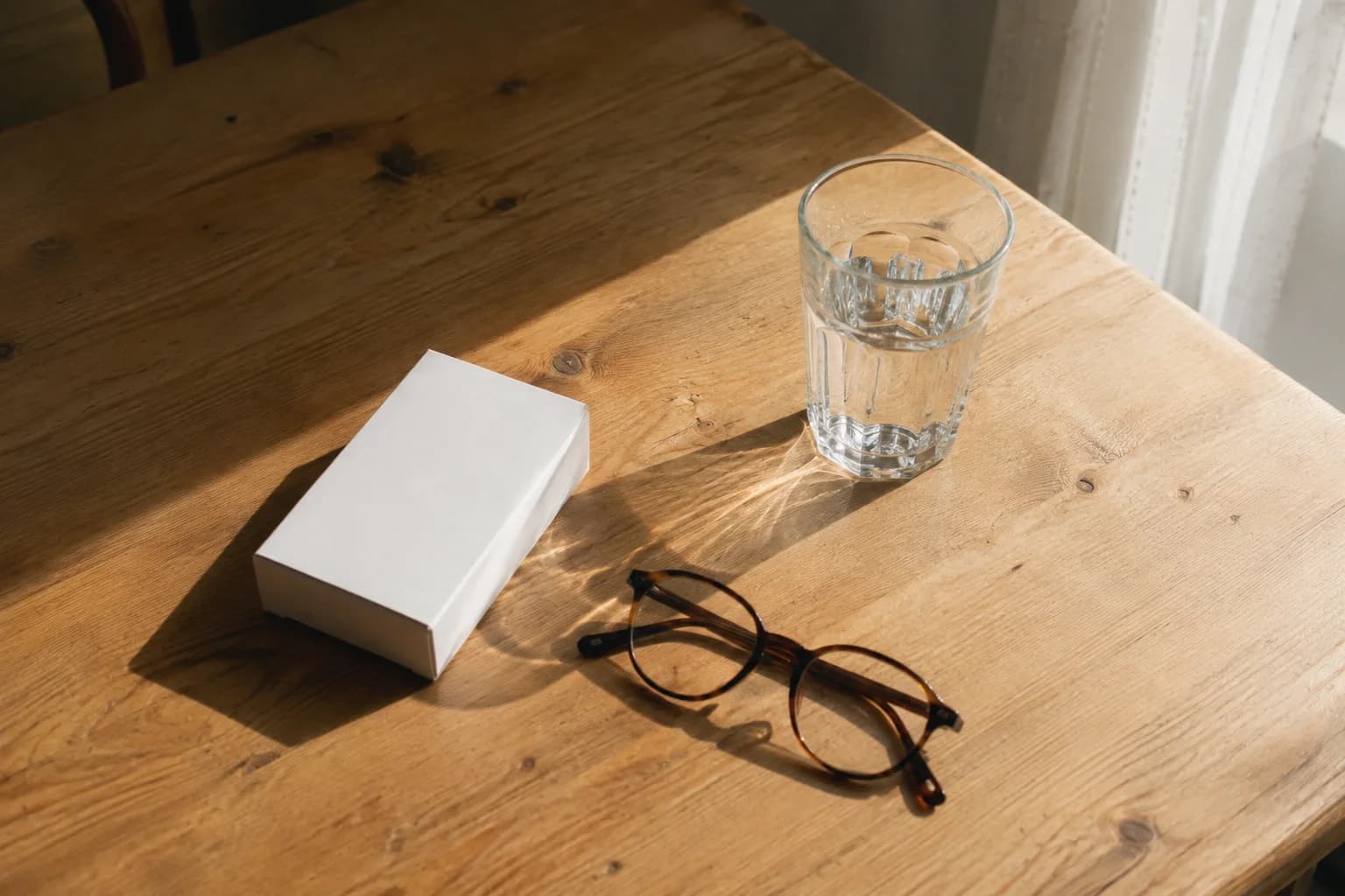 A medicine box beside a notebook, pen and glasses on a table
